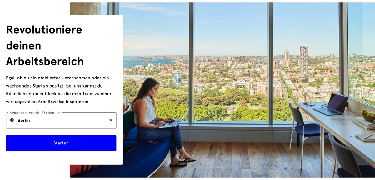 Frau arbeitet mit Laptop in modernem Büro mit großen Fenstern, Blick über eine grüne Stadtlandschaft, heller Raum mit Schreibtisch, Stühlen und ruhiger Arbeitsatmosphäre.