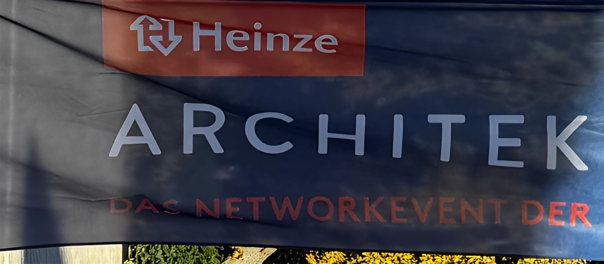 Banner mit der Aufschrift ‚Architektour‘ und dem Hinweis ‚Das Networkevent der Baubranche‘ vor blauem Hintergrund mit Lichtreflexen.