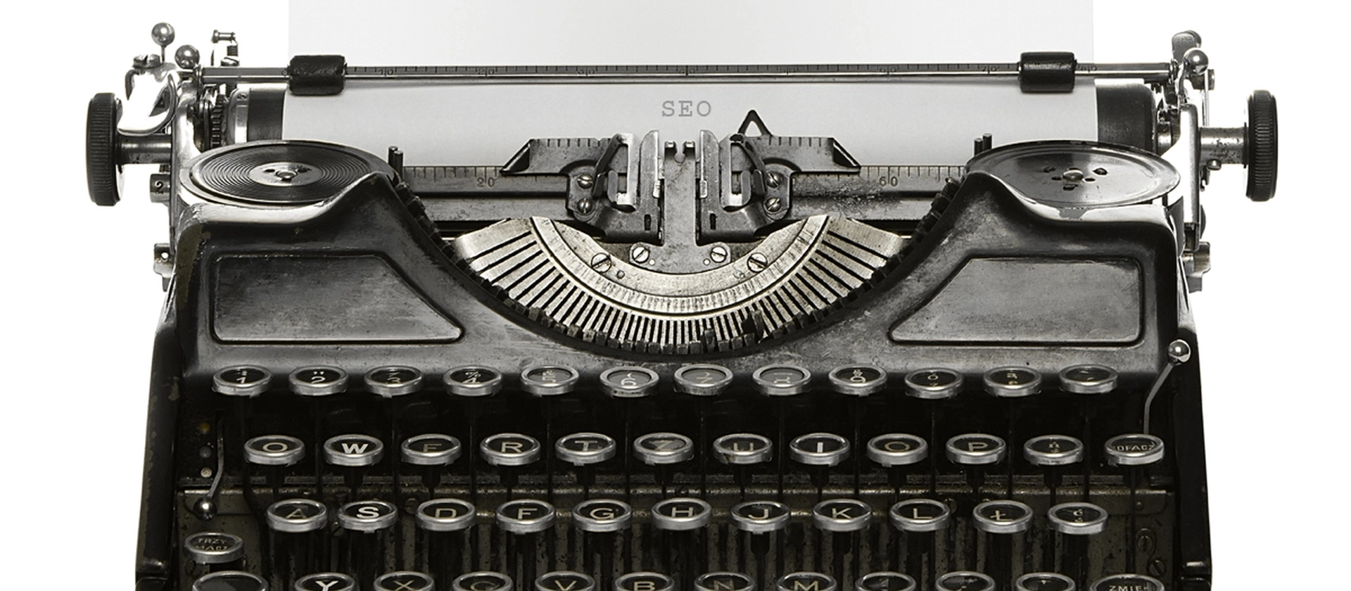 rontale Nahaufnahme einer alten schwarzen Schreibmaschine mit runden Tasten und sichtbarem Typenhebelmechanismus vor hellem, neutralem Hintergrund.