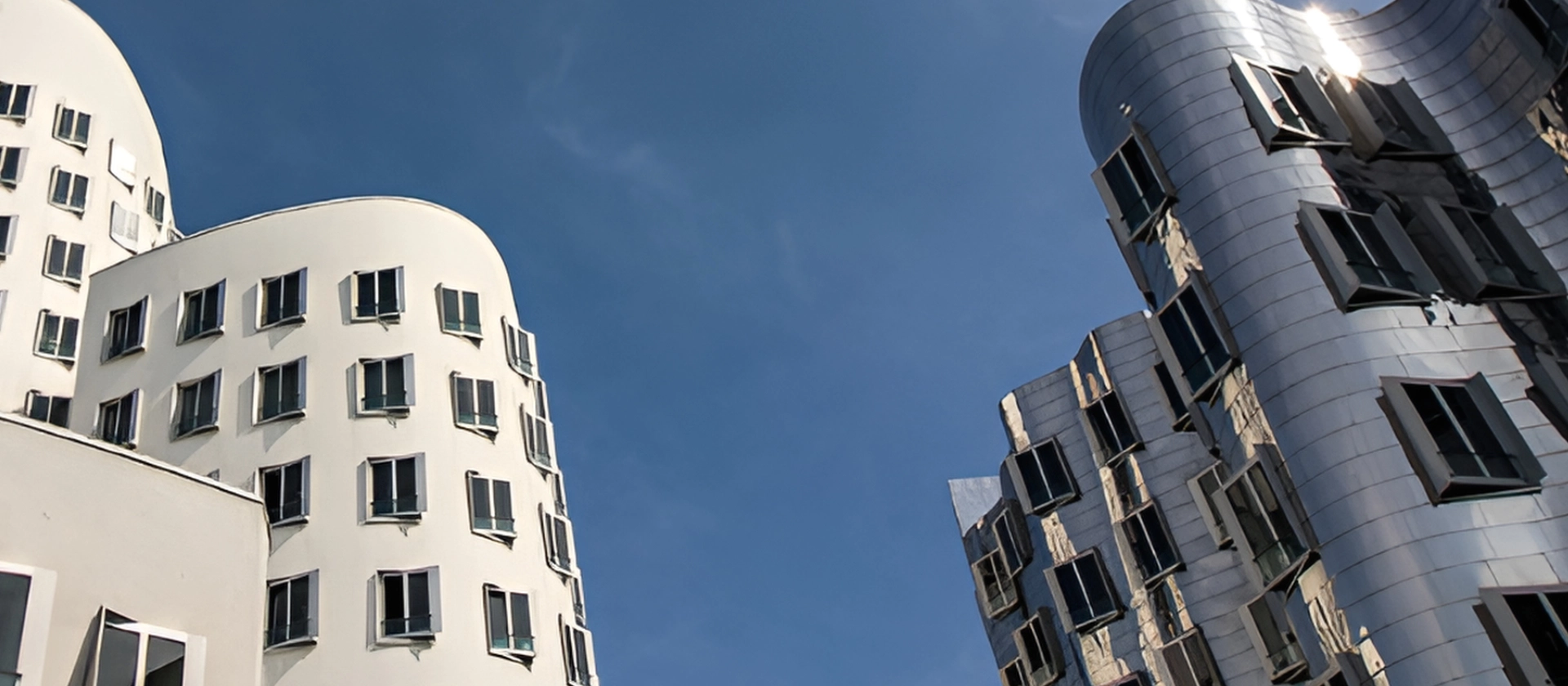 Moderne, geschwungene Bürogebäude mit weißen und metallisch glänzenden Fassaden ragen vor einem klaren, tiefblauen Himmel auf und wirken futuristisch und lichtdurchflutet.“