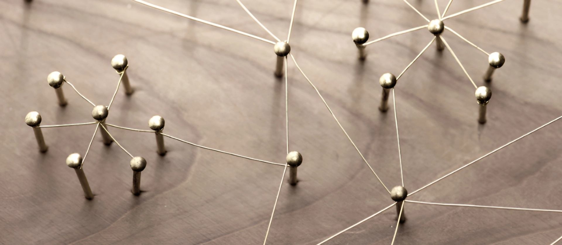 Metallene Stifte mit kugelförmigen Köpfen sind durch feine Drähte zu einem Netzwerk verbunden und liegen auf einer warmen Holzoberfläche, was Vernetzung und Beziehung symbolisiert.