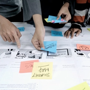 Hände von Personen, die während eines Workshops bunte Haftnotizen auf einer Customer Journey Map anordnen.
