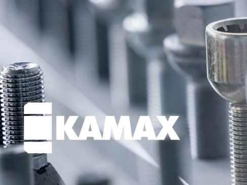 Das weiße Logo der Firma KAMAX, überlagert auf einer unscharfen Nahaufnahme von metallischen Befestigungselementen wie Schrauben und Bolzen mit Gewinde.