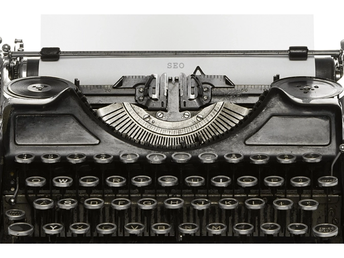 rontale Nahaufnahme einer alten schwarzen Schreibmaschine mit runden Tasten und sichtbarem Typenhebelmechanismus vor hellem, neutralem Hintergrund.