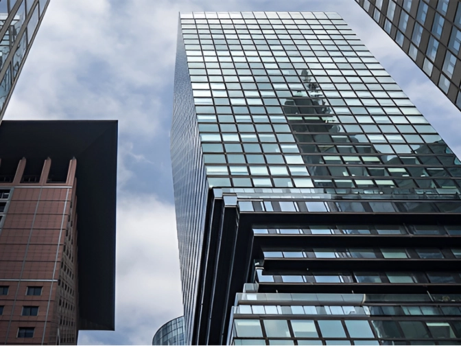 Blick von unten zwischen modernen Hochhäusern mit Glasfassaden und einem Backsteingebäude, die sich gegen einen bewölkten Himmel erheben