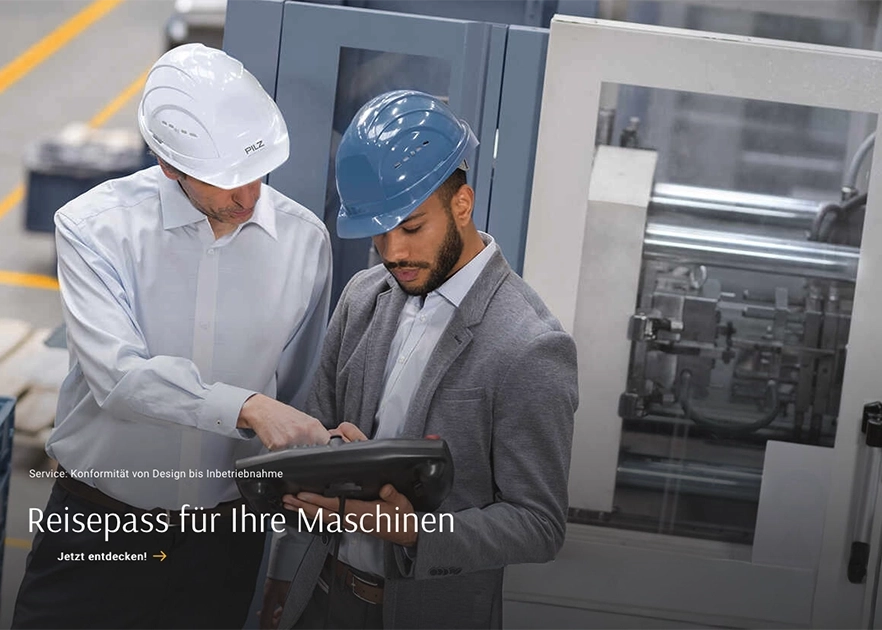 Zwei Experten mit Schutzhelmen prüfen ein Bediengerät an einer Maschine.