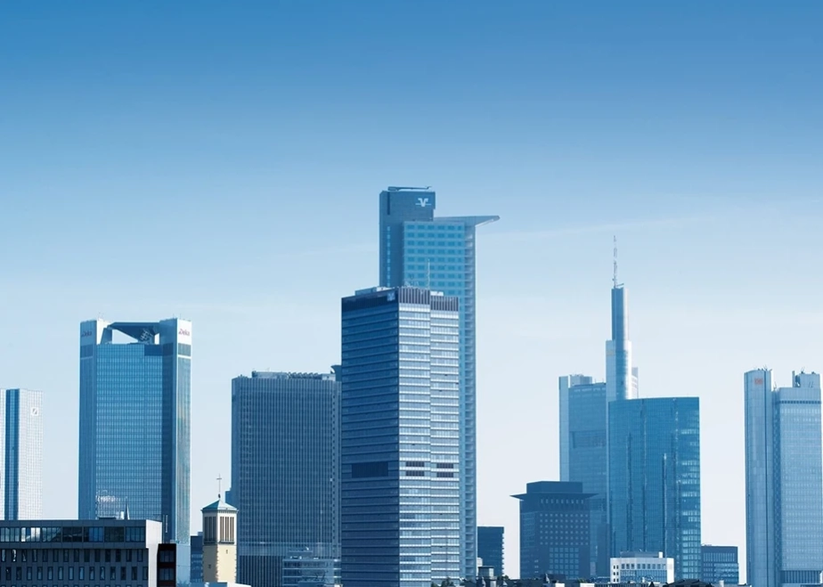 Panoramabild der Frankfurter Skyline mit mehreren modernen Hochhäusern, darunter das DZ Bank Gebäude und der Commerzbank Tower, unter einem klaren blauen Himmel.