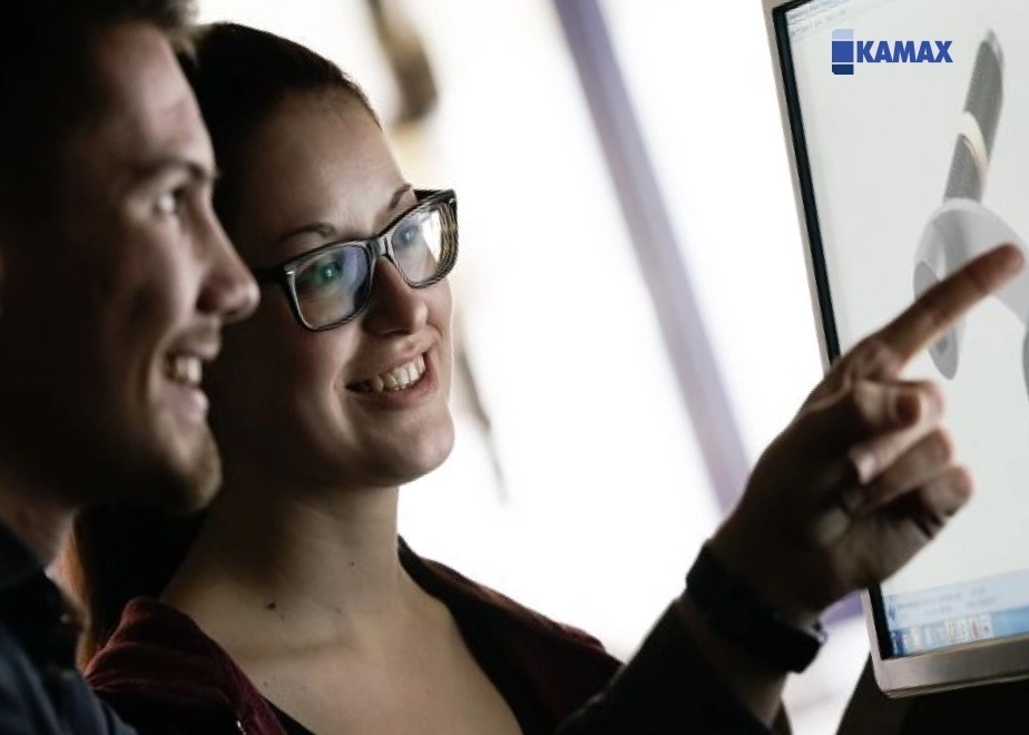 Screenshot der KAMAX Webseite. Im Bild zeigen zwei junge, lächelnde Mitarbeiter auf einen Bildschirm mit einem technischen 3D-Modell.